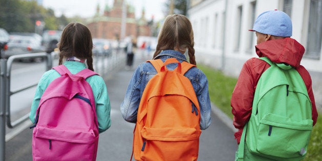 Backs of schoolkids with colorful rucksacks moving in the street