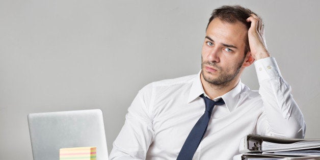 young business man sitting at messy desk, head in hand, depressed, overworked