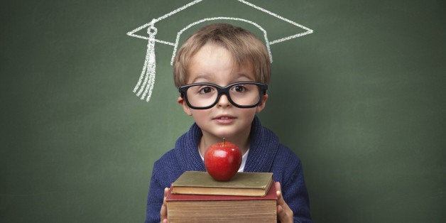 Child holding stack of books with mortar board chalk drawing on blackboard concept for university education and future aspirations