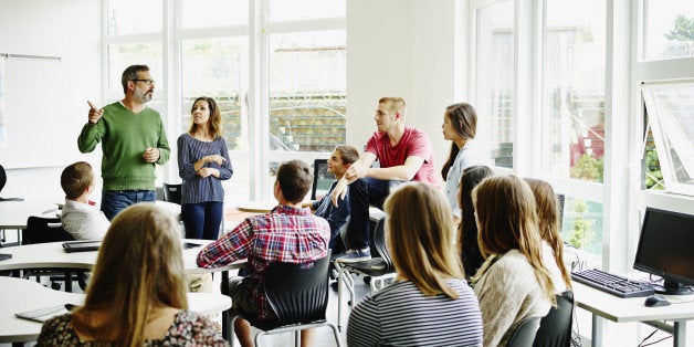 Two teachers standing in front of high school students giving instructions for project
