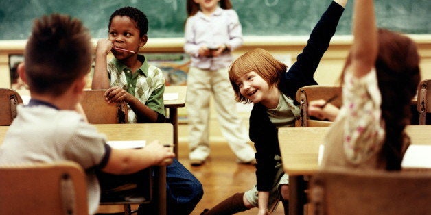 Children (6-8) in classroom, girls sitting at desk raising hands