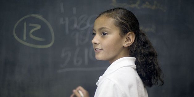 Ten year old Hispanic girl solves math problem in classroom.