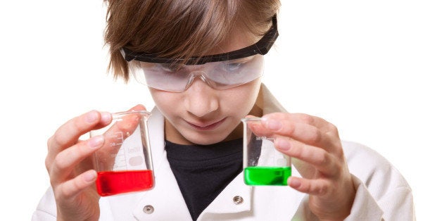 A close up of a 12 year old boy holding tow beakers of liquid as he compares them.