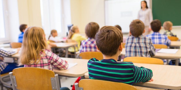 education, elementary school, learning and people concept - group of school kids sitting and listening to teacher in classroom from back