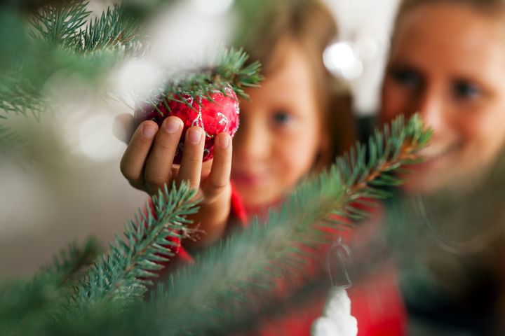 Young girl helping her mother decorating the Christmas tree, holding some Christmas baubles in her hand (Focus on bauble)