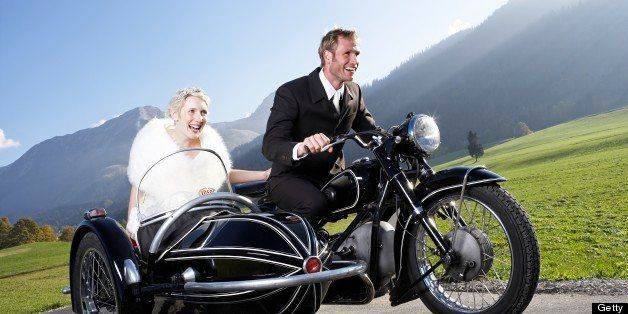Bride and groom riding motorcycle with sidecar in rural area