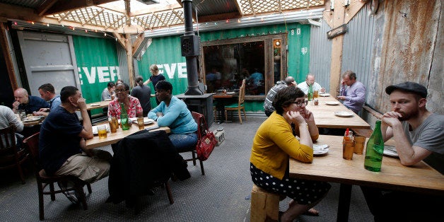 Patrons sit in an industrial-style courtyard where the walls are formed from pieces of metal shipping containers at Roberta's, the most popular of a crop of trendy restaurants in Brooklyn's cutting-edge Bushwick neighborhood Tuesday, April 22, 2014, in New York. (AP Photo/Kathy Willens)