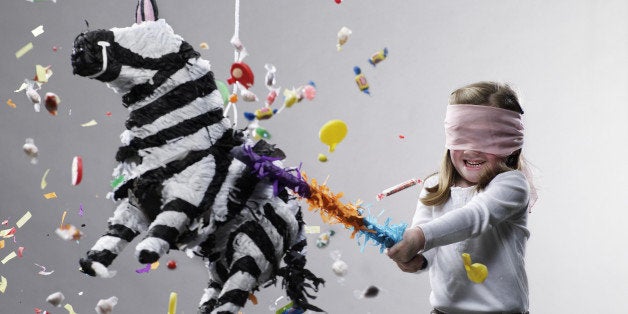 Young girl hitting pinata, candy flying