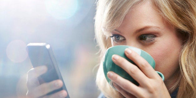 Woman using phone and drinking coffee.