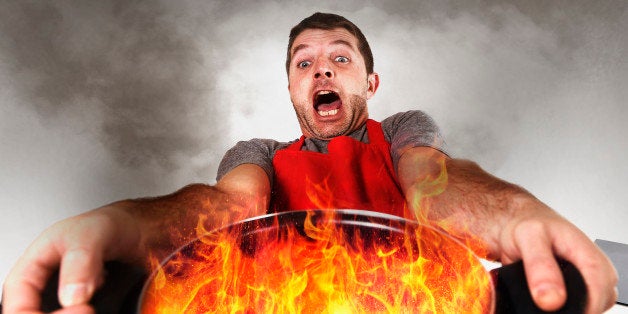 young inexperienced home cook with apron holding pot burning in flames with stress and panic face expression in fire in the kitchen and cooking wrong concept