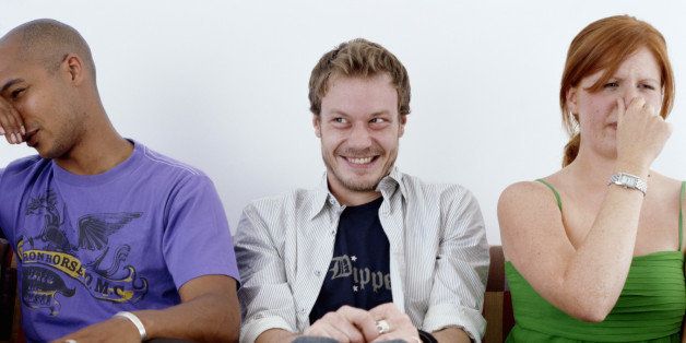Young man, smiling, sitting between man and woman holding noses