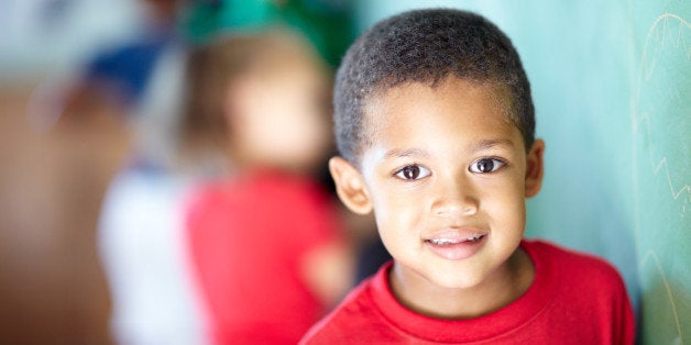 Sweet little boy standing at the chalkboard in a classroom