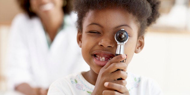 Girl (6-7) looking through otoscope, female doctor smiling background