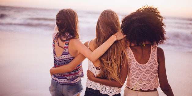 Rear view of an Afro girl and friends walking with their arms round each other closely on the beach at dusk