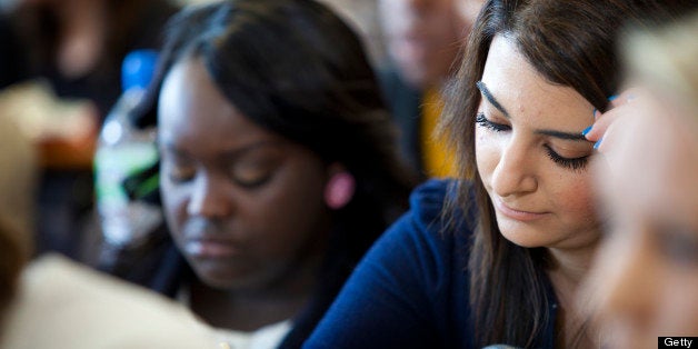 Selective focus and a low angle shot through the faces of a crowd of university students sitting in class concentrating on their work.