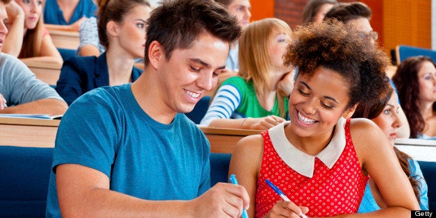 Large group of students sitting in the lecture hall at university. Focus on the cheerful young man and woman working together.