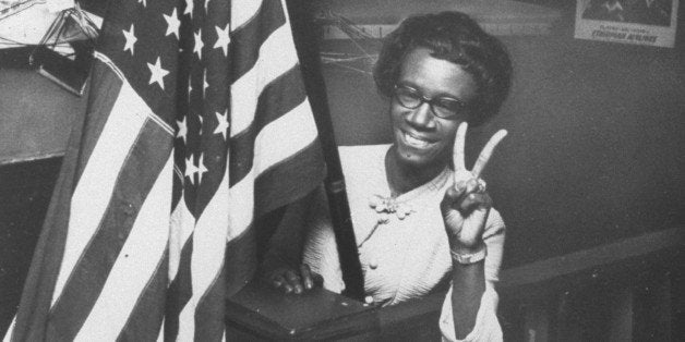 1st black female member of Congress, Shirley Chisholm, holding up two fingers in victory sign while standing behind large American flag following her successful run for office. (Photo by Fred De Van//Time Life Pictures/Getty Images)