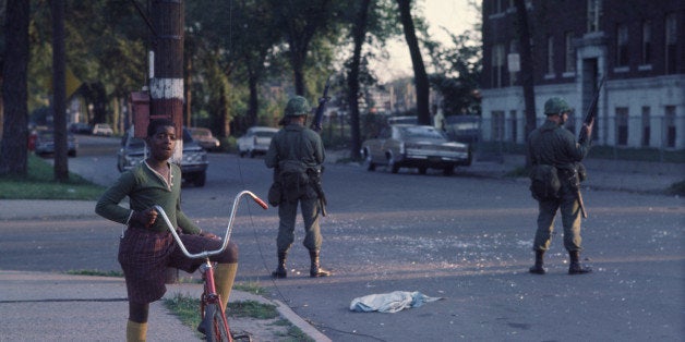 National Guardsmen stand guard as a young boy pauses from riding his bicycle in the west side neighborhood of Lawndale, Chicago, 1968. The guardsmen were called in to restore order after the rioting that occured as a result of Martin Luther King, Jr.'s assassination, 1968. (Photo by Chicago History Museum/Getty Images)