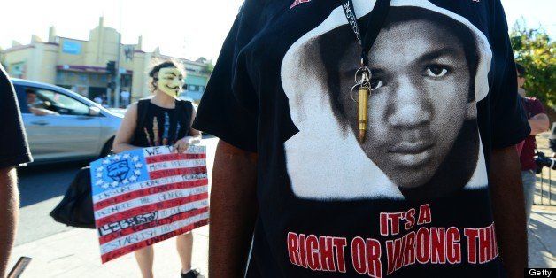 A man wears a single bullet around his neck over his Trayvon t-shirt as people hold placards and shout slogans during a rally in Los Angeles in the aftermath of George Zimmerman's acquittal in the shooting death of Florida teen Trayvon Martin, on July 15, 2013 in California, where local civil rights activists and other leaders urged participants to remain peaceful as they express frustration with the trial's outcome. AFP PHOTO/Frederic J. BROWN (Photo credit should read FREDERIC J. BROWN/AFP/Getty Images)