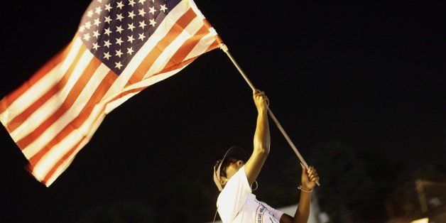A demonstrator protesting the shooting of Michael Brown waves the American flag August 21, 2014 in Ferguson, Missouri. Crowds continue to gather to march along Florissant Road after Brown was fatally shot by Ferguson Police Officer Darren Wilson August 9th. AFP PHOTO/Joshua LOTT (Photo credit should read Joshua LOTT/AFP/Getty Images)