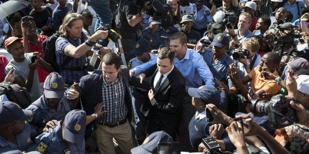 South African Paralympic athlete Oscar Pistorius (C) is surrounded by members of the media as he leaves the High Court after the verdict hearing of his trial over the killing of his model girlfriend Reeva Steenkamp, on September 11, 2014 in Pretoria. Oscar Pistorius was found not guilty of murdering his girlfriend Reeva Steenkamp, a shock decision that left the South African celebrity athlete sobbing with emotion in the dock. The high-profile trial was adjourned until Friday when the 27-year-old Paralympian will hear whether he has been found guilty of culpable homicide, a lesser charge roughly equivalent to manslaughter. AFP PHOTO/MUJAHID SAFODIEN (Photo credit should read MUJAHID SAFODIEN/AFP/Getty Images)