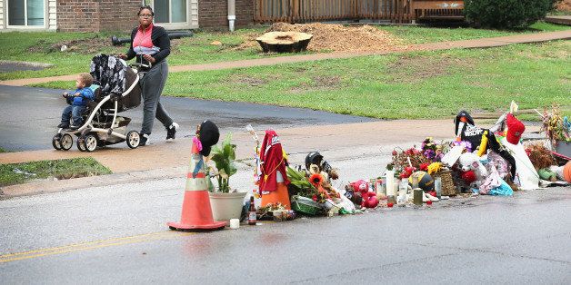 FERGUSON, MO - SEPTEMBER 10: Ashley Haynes pushes her son Ashten past a rain-soaked memorial which remains in the middle of the road where teenager Michael Brown died after being shot by Ferguson police officer Darren Wilson about a month ago on September 10, 2014 in Ferguson, Missouri. Although the violence, which erupted in the city following the shooting, has subsided residents continue to protest for a change in the city leadership and against racial profiling by the police. (Photo by Scott Olson/Getty Images)