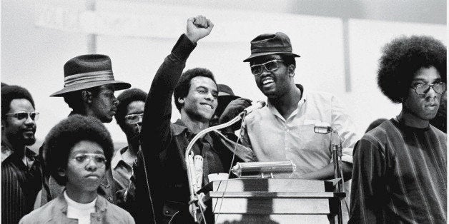 Black Panther Party co-founder Huey P. Newton (1942 - 1989) (center) smiles as he raises his fist from a podium at the Revolu
