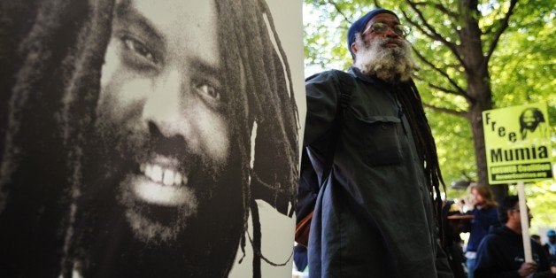 A protestor stands next to an image of Mumia Abu-Jamal outside the US Department of Justice on April 24, 2012 in Washington, DC, calling for the release from prison of the ex-Black Panther militant, who was convicted for the killing of a white police officer in 1981 and sentenced to death. In December 2011 prosecutors gave up their effort to execute Abu-Jamal, who supporters believe is innocent and was framed for the murder in the racially charged case. Supporters decided to hold their demonstration on April 24, 2012, Abu-Jamal's 58th birthday. AFP PHOTO / Mandel NGAN (Photo credit should read MANDEL NGAN/AFP/Getty Images)