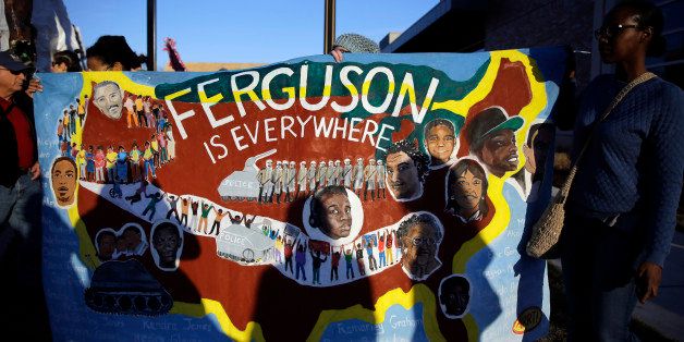 People hold up a sign during a protest outside the Ferguson Police Department, Monday, Jan. 19, 2015, in Ferguson, Mo. Protesters marched several miles through Ferguson to the police department from the site where Michael Brown was killed this past summer by a police officer. (AP Photo/Jeff Roberson)
