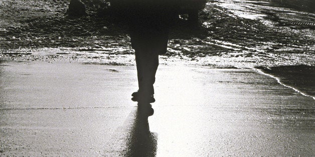 Silhouette of person standing on wet sidewalk at night