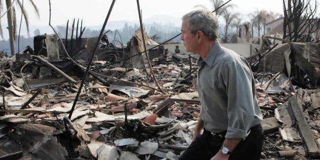 US President George W. Bush tours the remnants of a home after it was hit by a wildfire in San Diego, California, 25 October 2007. Bush viewed some of the hardest-hit areas during a helicopter tour, visited a neighborhood of San Diego, and met with rescue workers, firefighters and Governor Arnold Schwarzenegger. The president's swift visit to California comes two years after he was accused of responding sluggishly to devastation in New Orleans after Hurricane Katrina. AFP PHOTO/SAUL LOEB (Photo credit should read SAUL LOEB/AFP/Getty Images)