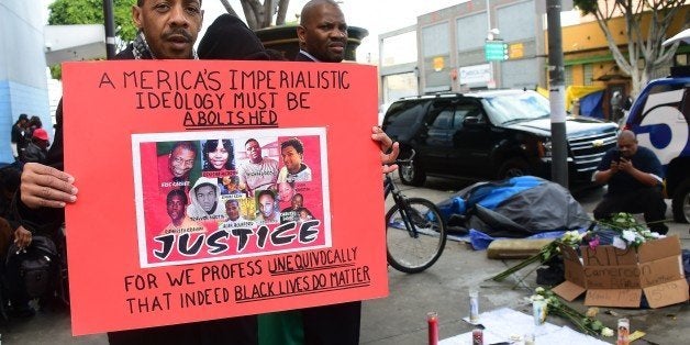 Eddie Howard holds a placard reading 'America's Imperialistic Idealogy Must Be Abolished' near a makeshift memorial for a homeless man known by the name of 'Africa,' who was shot and killed by LA police on March 2, 2015 in Los Angeles, California. Los Angeles police fatally shot a the man March 1, in an incident that was caught on video and circulated widely online, with the department saying officers resorted to deadly force after the man had reached for one of their guns. The graphic footage, which appeared on Facebook, shows a violent altercation between a man and several officers in LA's 'Skid Row,' an area near downtown where many homeless people live. bThe video appears to show the man flailing at officers as they try to subdue him. AFP PHOTO/ FREDERIC J. BROWN (Photo credit should read FREDERIC J. BROWN/AFP/Getty Images)