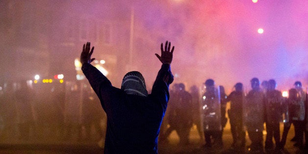 A protestor faces police enforcing a curfew Tuesday, April 28, 2015, in Baltimore. A line of police behind riot shields hurled smoke grenades and fired pepper balls at dozens of protesters to enforce a citywide curfew. (AP Photo/Matt Rourke)