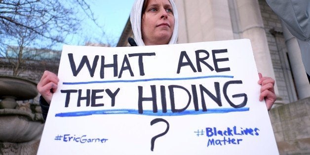 A protester displays a placard during a demonstration outside the courthouse in New York's borough of Staten Island on January 5, 2015, before a hearing in a state lawsuit seeking the release of grand jury proceedings concerning the death of Eric Garner. Garner, a father of six who was suspected of illegally selling cigarettes, was wrestled to the ground by several white police officers after resisting arrest on Staten Island on July 17, 2014. Classified as a homicide by the New York medical examiner's office, his death set off intense reactions and several protests in New York reminiscent of those in Ferguson, Missouri, over the August 9 police shooting of unarmed black teenager Michael Brown. AFP PHOTO/JEWEL SAMAD (Photo credit should read JEWEL SAMAD/AFP/Getty Images)