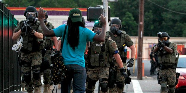 Police wearing riot gear point their weapons before arresting a man Monday, Aug. 11, 2014, in Ferguson, Mo. The shooting death of Michael Brown, 18, an unarmed black man by a white police officer sparked protests and other civil unrest. (AP Photo/Jeff Roberson)