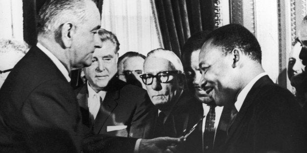 U.S. President Lyndon B. Johnson hands a pen to civil rights leader Rev. Martin Luther King Jr. during the the signing of the voting rights act as officials look on behind them, Washington, D.C., August 6, 1965. (Photo by Washington Bureau/Getty Images)