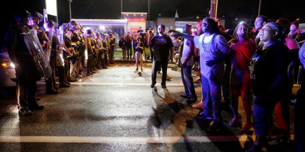 Protesters yell as police form a line across West Florissant Ave., Sunday, Aug. 9, 2015, in Ferguson, Mo., before shots were fired near the protest. The one-year anniversary of Michael Brown's death in Ferguson began with a march in his honor and ended with a protest that was interrupted by gunfire. (AP Photo/Jeff Roberson)