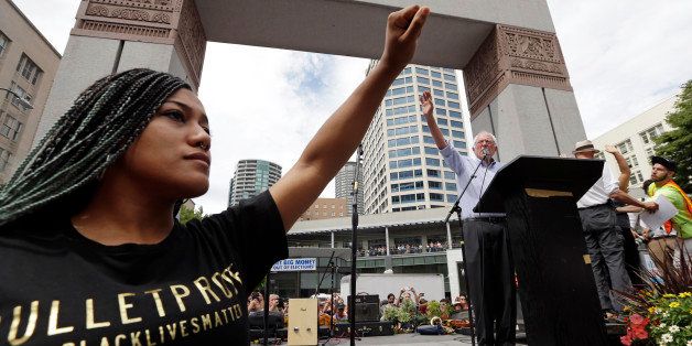 Mara Jacqueline Willaford, left, holds her fist overhead as Democratic presidential candidate Sen. Bernie Sanders, I-Vt., waves to greet the crowd before speaking at a rally Saturday, Aug. 8, 2015, in downtown Seattle. Willaford and another co-founder of the Seattle chapter of Black Lives Matter took over the microphone just after Sanders began to speak and refused to relinquish it. Sanders eventually left the stage without speaking further and instead waded into the crowd to greet supporters. (AP Photo/Elaine Thompson)