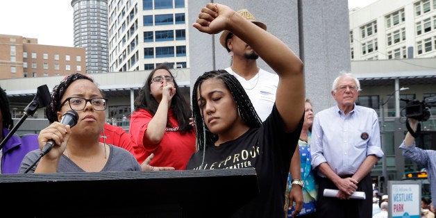 Marissa Johnson, left, speaks as Mara Jacqueline Willaford holds her fist overhead and Democratic presidential candidate Sen. Bernie Sanders, I-Vt., stands nearby as the two women take over the microphone at a rally Saturday, Aug. 8, 2015, in downtown Seattle. The women, co-founders of the Seattle chapter of Black Lives Matter, took over the microphone and refused to relinquish it. Sanders eventually left the stage without speaking and instead waded into the crowd to greet supporters. (AP Photo/Elaine Thompson)