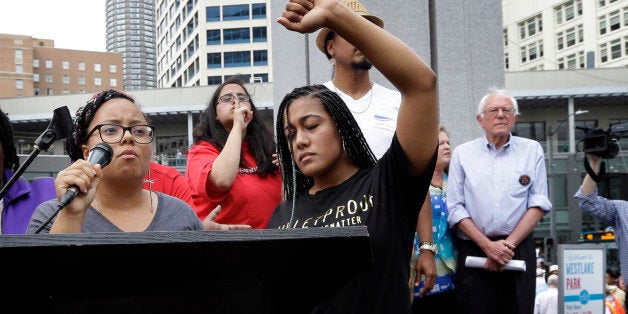 Marissa Johnson, left, speaks as Mara Jacqueline Willaford holds her fist overhead and Democratic presidential candidate Sen. Bernie Sanders, I-Vt., stands nearby as the two women take over the microphone at a rally Saturday, Aug. 8, 2015, in downtown Seattle. The women, co-founders of the Seattle chapter of Black Lives Matter, took over the microphone and refused to relinquish it. Sanders eventually left the stage without speaking and instead waded into the crowd to greet supporters. (AP Photo/Elaine Thompson)