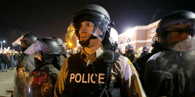 FILE- In this Nov. 25, 2014 file photo, police watch the street as protesters gather outside the Ferguson Police Department i