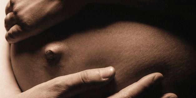 Pregnant woman holding bump, close-up (toned B&W)