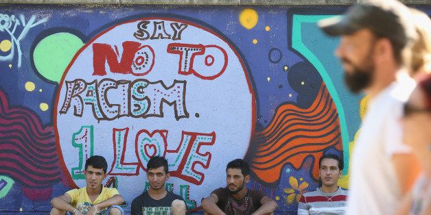 MUNICH, GERMANY - AUGUST 29: Migrants from Syria with non-alcoholic drinks sit under a mural that reads: 'Say No To Racism. 1 Love' at a summer fest for migrants seeking asylum in Germany and locals at the Bayernkaserne asylum shelter on August 29, 2015 in Munich, Germany. The Bayernkaserne is a former military barracks currently home to approximately 1,000 foreign migrants. Germany is expecting to receive 800,000 asylum-seeking migrants this year and is struggling to cope with the record number. (Photo by Sean Gallup/Getty Images)