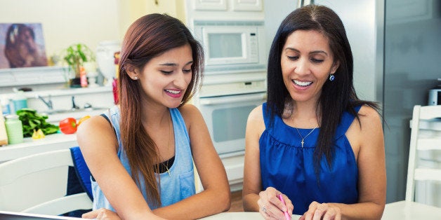 Mother and teenage daughter are in the kitchen researching colleges and filling out university applications.