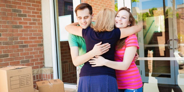 Family hugging and saying goodbye to college students moving dormitory in a university campus. Mother emotional goodbye to college children, group hugging the young adult in front of the dormitory apartment, surrounded by boxes and luggage. Photographed on location in horizontal format. Location, USA