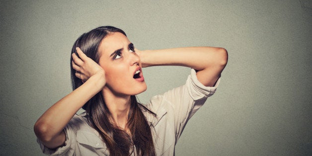 Portrait young annoyed, unhappy, stressed woman covering her ears, looking up, to say, stop making loud noise, giving me headache isolated grey background with copy space. Negative emotion reaction