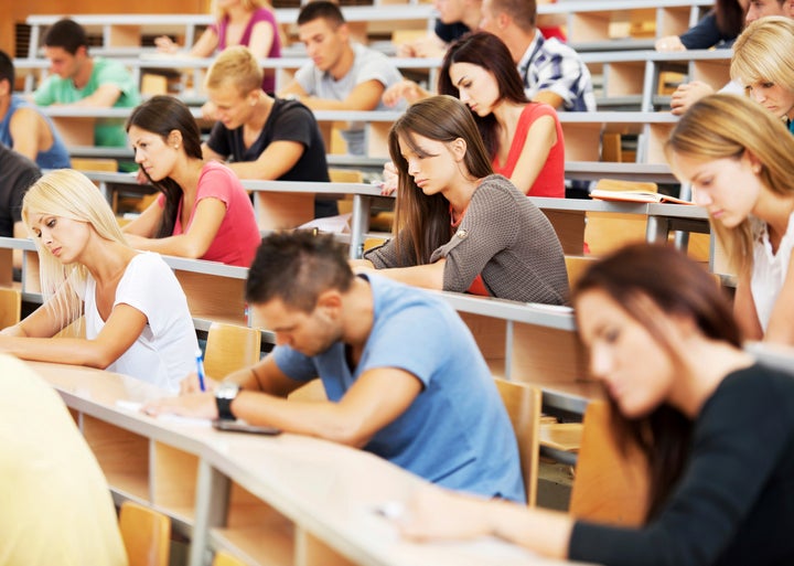 Group of college students in the university amphitheatre, they are sitting and doing an exam.