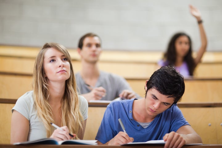 Students taking notes while their classmate is raising her hand in an amphitheater