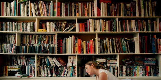 Young woman lying on floor by book shelves, reading, side view