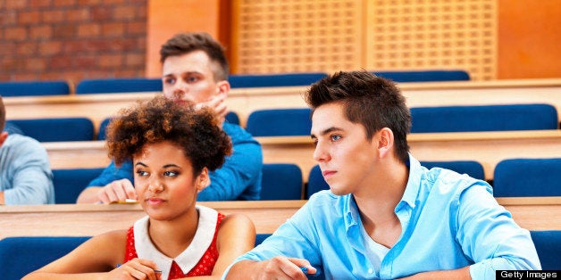 High school students sitting in the lecture hall at university and listening to a lecture, looking bored.